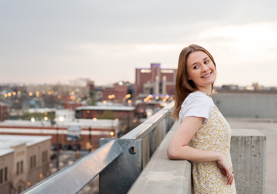 high school senior girl leans against an outer wall of a parking garage rooftop in Oklahoma City and smiles over shoulder