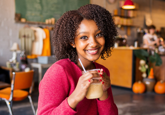 Ethiopian teen girl wearing a pink sweater sits in a coffee shop in Norman Oklahoma holding her iced coffee drink and smiling