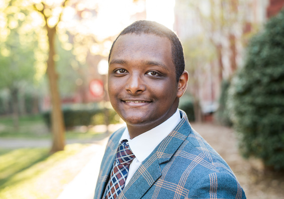 Close up portrait of an African-American high school senior boy wearing a plaid suit standing on a sidewalk between buildings on the OU campus in Norman, Oklahoma