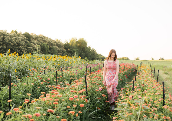 High school senior girl walks and holds her dress through a flower farm field in Oklahoma