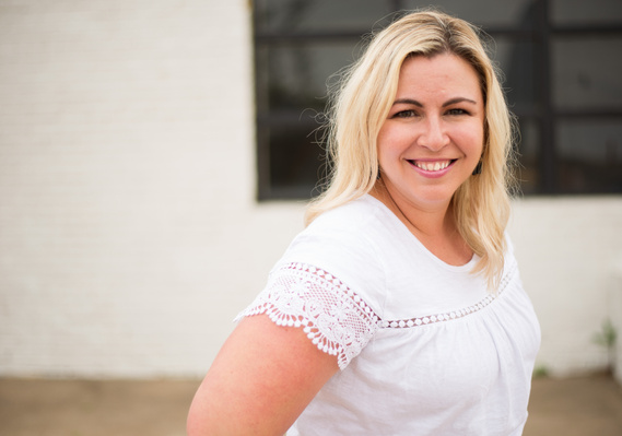 headshot of a photographer, blond woman in a white shirt smiling in front of a industrial building in Oklahoma City