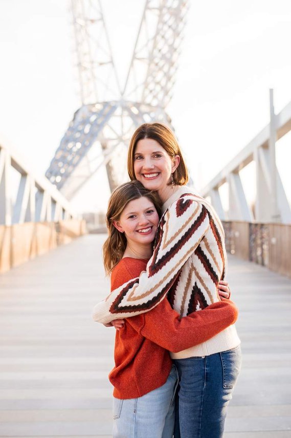 a mom and her teen daughter stand and hug together on the Skydance Bridge  at Scissortail Park in Oklahoma City 