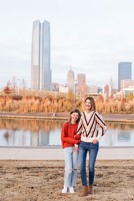 a mom and her teen daughter stand and hug together laughing at Scissortail Park in Oklahoma City with the downtown buildings behind them