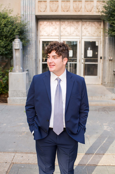 senior boy in a blue suit stands with hands in pocket in front of OKC courthouse in downtown smiling