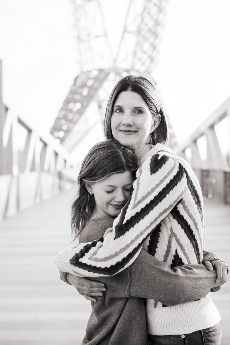 a mom and her teen daughter hug each other in a black and white photo on the Skydance Bridge at Scissortail Park in Oklahoma City