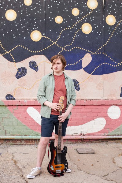 senior boy stands with his bass guitar in front of a wall mural in Oklahoma City