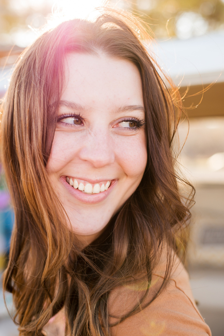 close up portrait of a high school senior girl with long brown hair smiling to the side with a colorful sun flare around her in Tuttle Oklahoma
