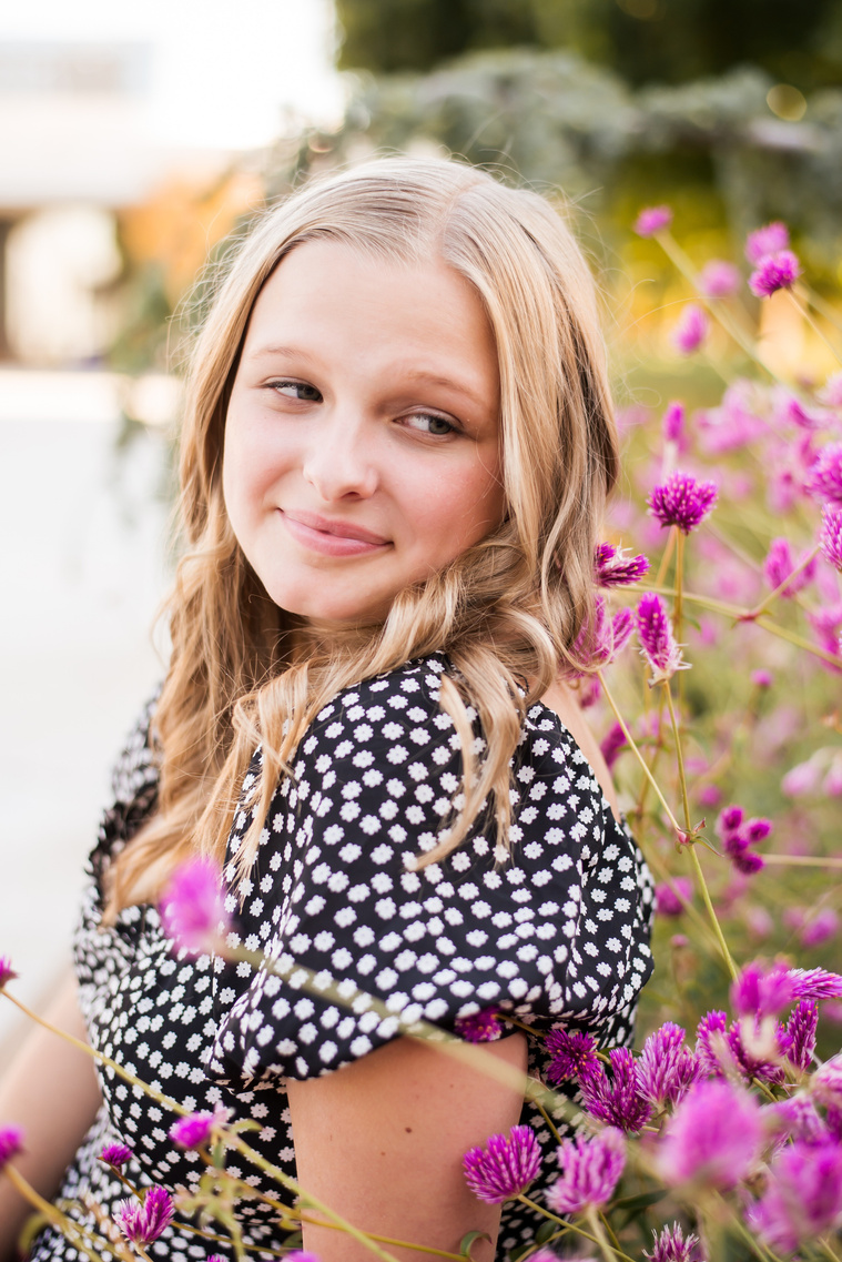 blond high school senior girl wearing a dress sitting among pink flowers for senior pictures at Myriad Gardens in downtown Oklahoma City