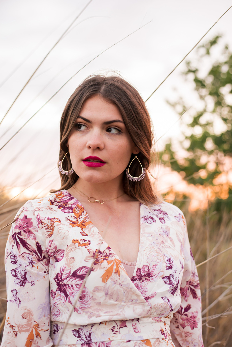 high school senior girl dressed in boho style stands and looks off with a serious expression in a field with tall golden grass around her in Oklahoma City, Oklahoma