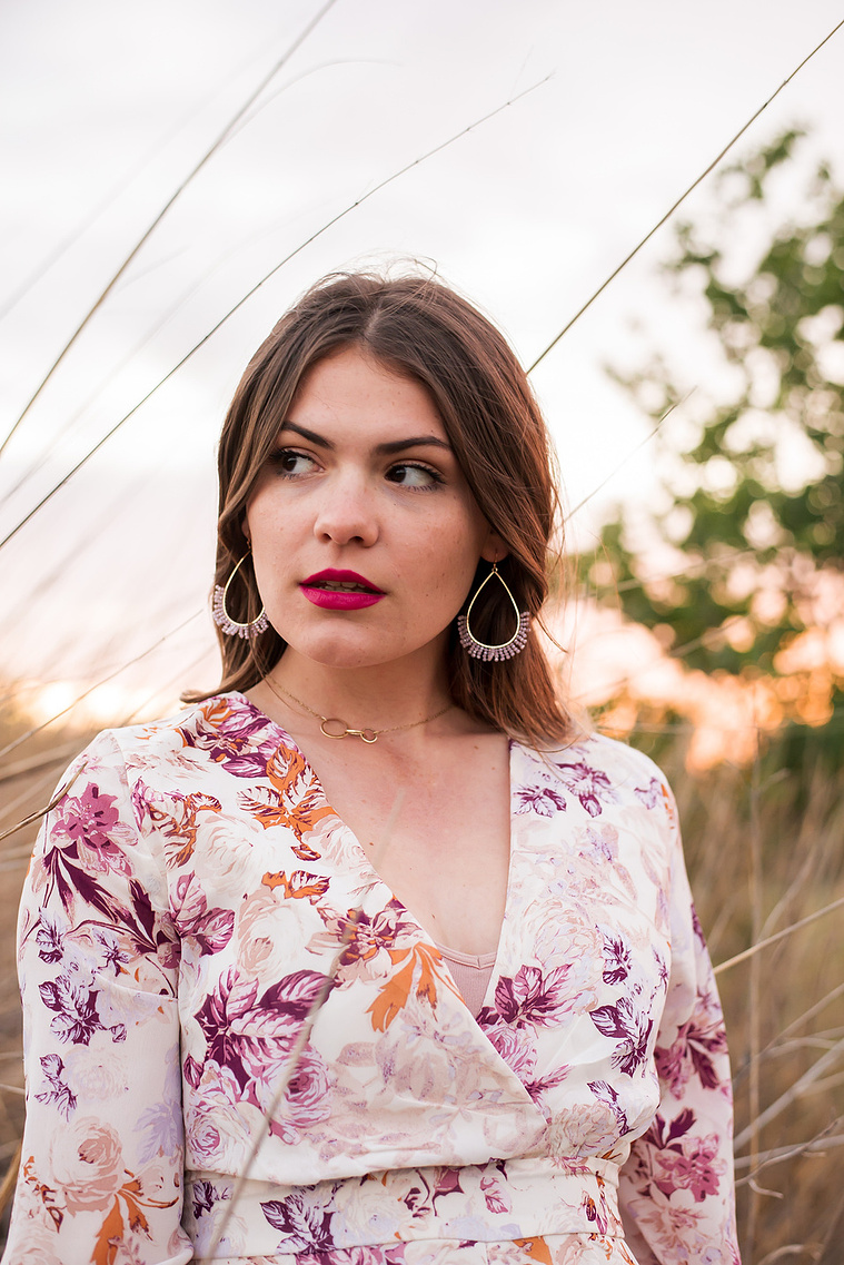 high school senior girl dressed in boho style stands and looks off with a serious expression in a field with tall golden grass around her in Oklahoma City, Oklahoma