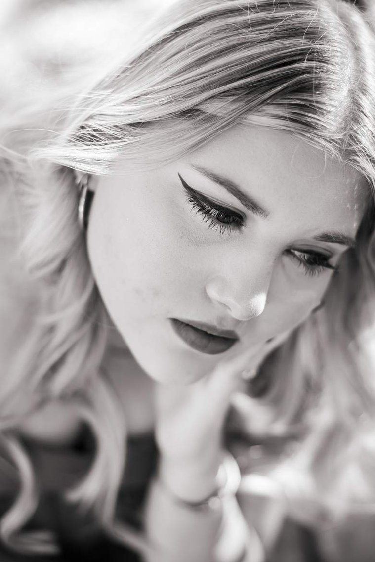 close up portrait of  a high school senior girl resting her chin in her hand and looking down and to side with a soft smile in downtown Oklahoma City