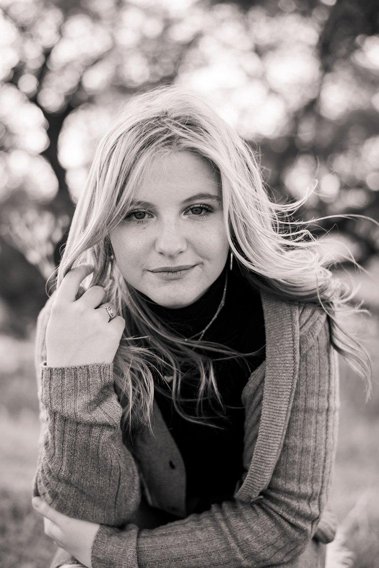 black and white photo of a high school senior girl holding one elbow and the tip of her hair looking softly serious at camera at a photo session in Oklahoma