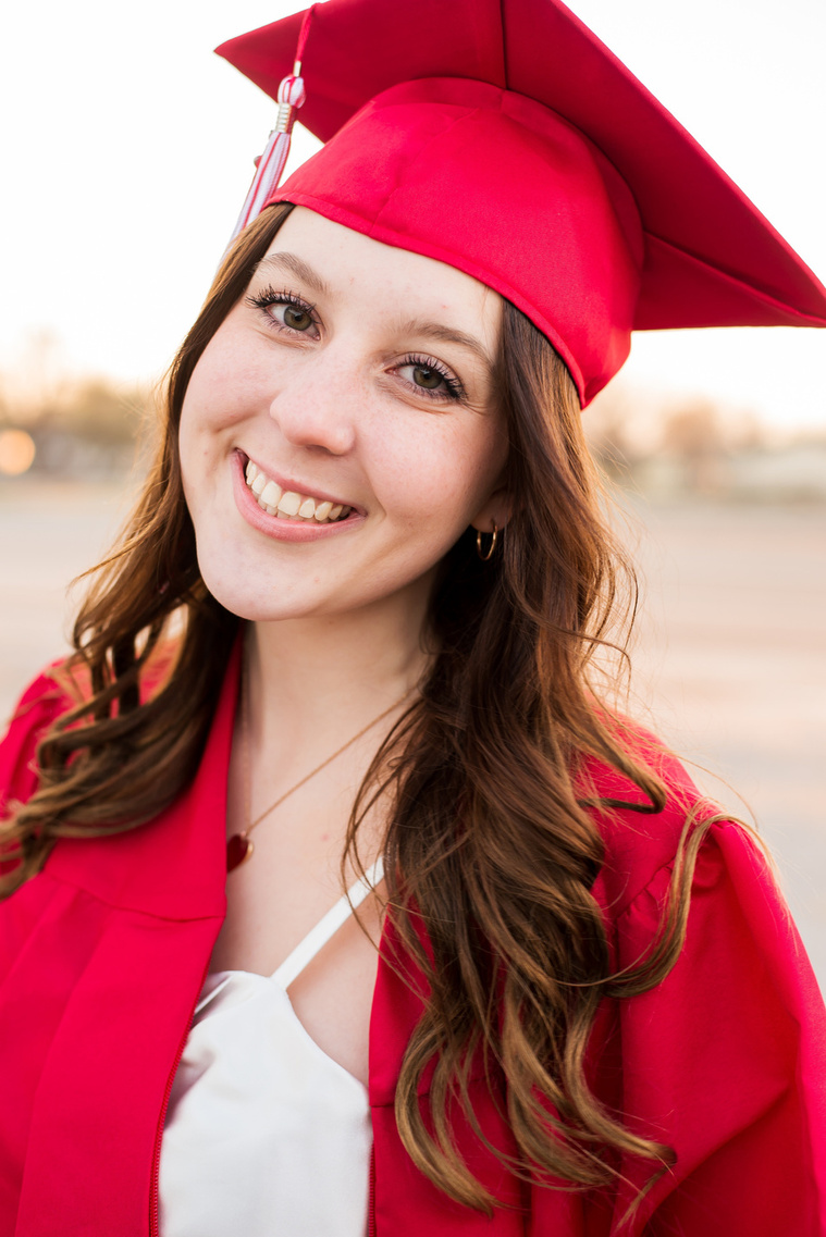 portrait of a high school senior girl wearing a white dress and her red cap and gown smiling in Tuttle Oklahoma
