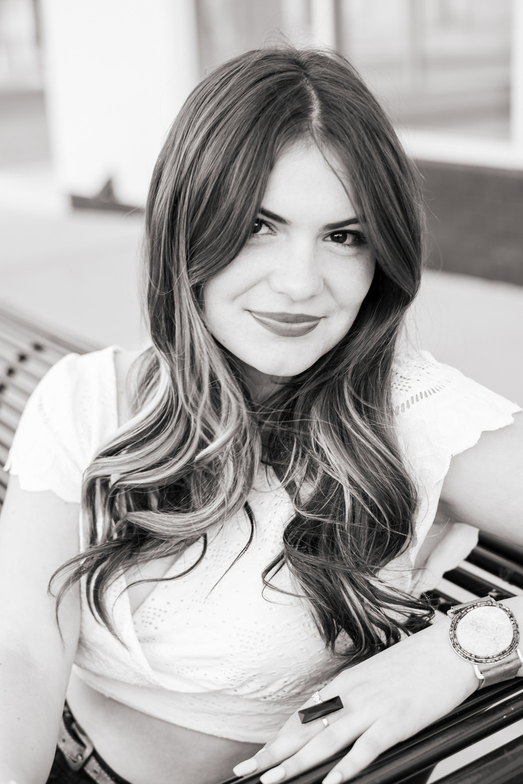 close up black and white portrait of a high school senior girl with long hair sitting on a bench on the sidewalk in Automobile Alley in Oklahoma City, Oklahoma