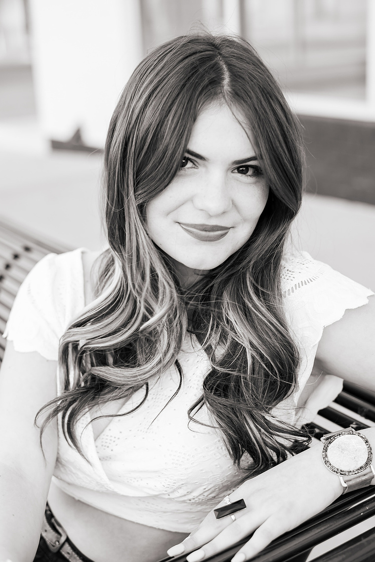 close up black and white portrait of a high school senior girl with long hair sitting on a bench on the sidewalk in Automobile Alley in Oklahoma City, Oklahoma