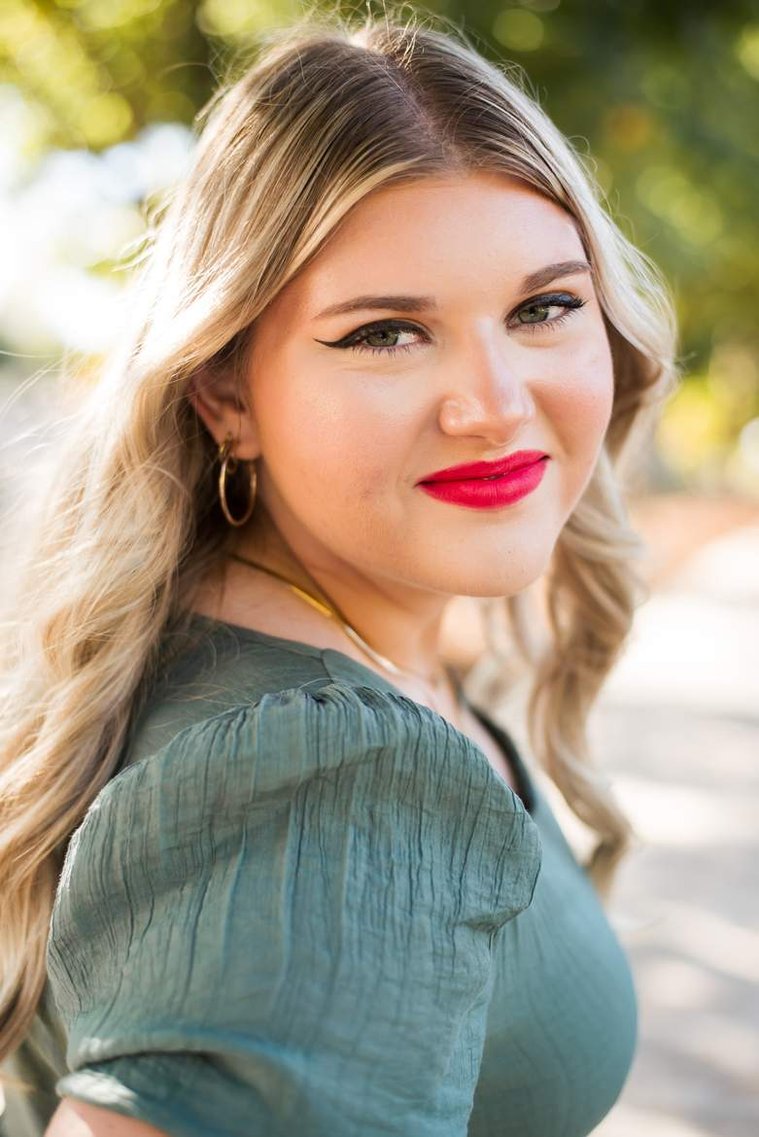 blond high school senior girl wearing a green dress smiles over her shoulder at Myriad Gardens in downtown Oklahoma City for senior portraits