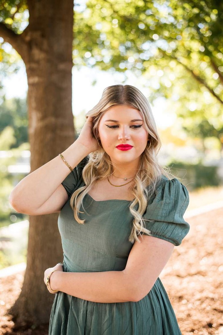 blond high school senior girl with one hand in hair, other wrapped around her waist in a green dress looking down at Myriad Gardens in downtown Oklahoma City for senior portraits
