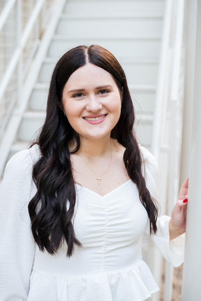 college senior girl poses for a headshot wearing a white top standing in front of white stairs on the campus of University of Oklahoma in Norman