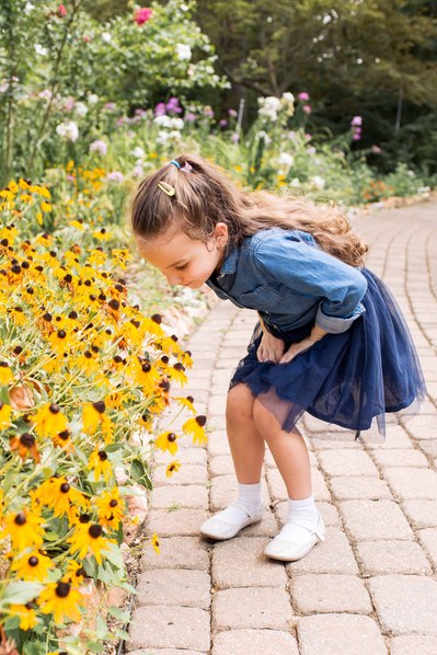 a little girl stoops down to smell the yellow flowers along a path at Lendonwood Gardens in Grove, Oklahoma.