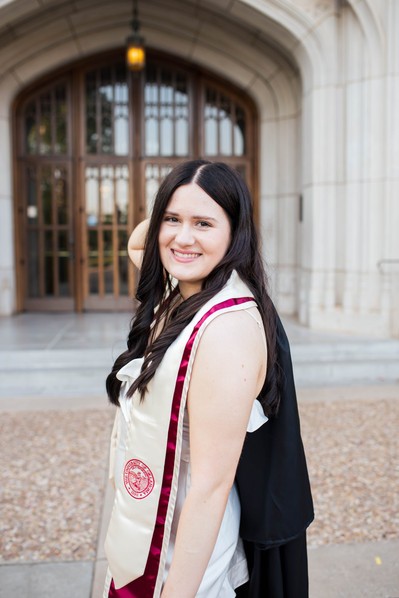 college senior girl poses in front of the library doors with graduation gown over her shoulder smiling on the OU campus in Norman