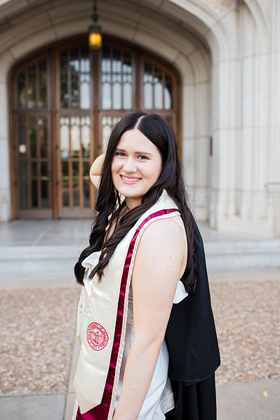 college senior girl poses in front of the library doors with graduation gown over her shoulder smiling on the OU campus in Norman
