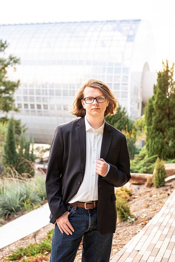 senior boy wearing a sport coat and jeans stands casually in front of the Crystal Bridge at Myriad Gardens in OKC