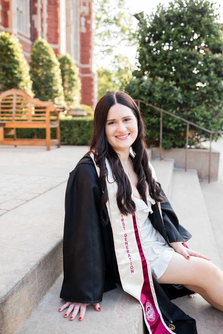 college senior wearing her graduation gown and stole, sits on the steps of the OU library on campus in Norman, Oklahoma