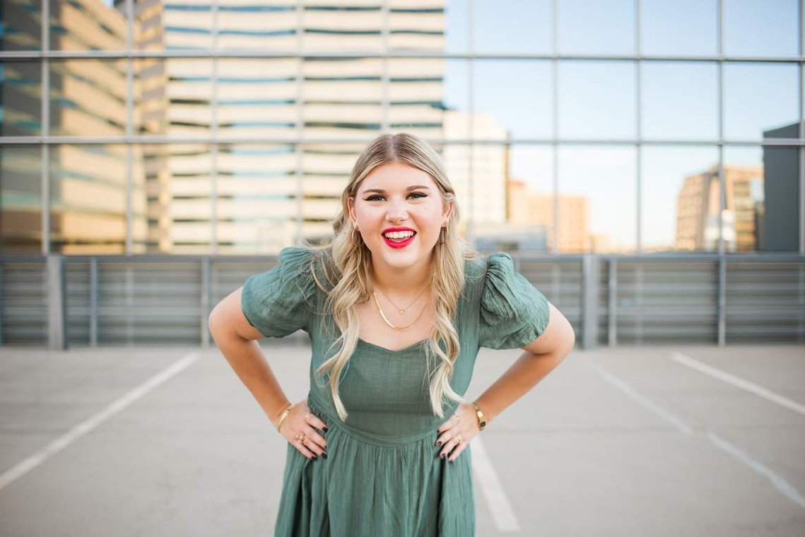 blond high school senior girl stands with her hands on her hips in a green dress on top of the devon tower parking garage in okc