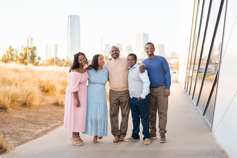 Ethiopian family standing together by the Devon Boathouse in Oklahoma City hugging and smiling with the skyline behind them for family photos