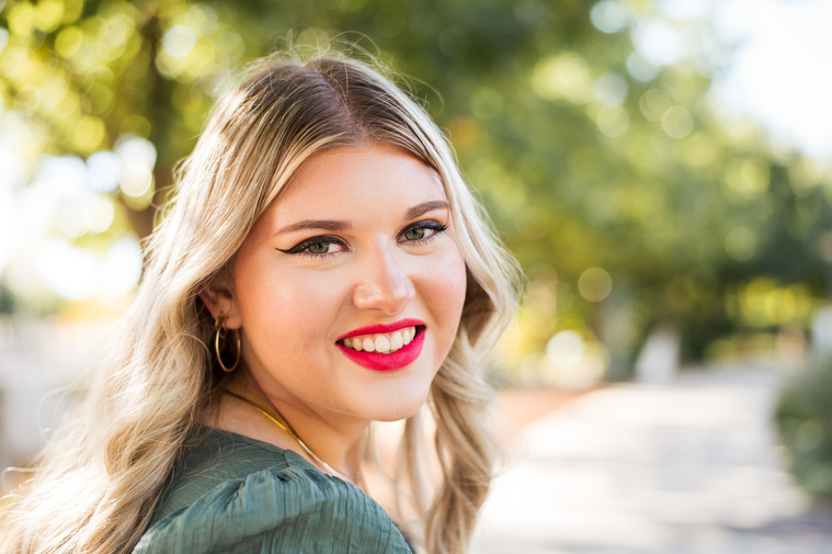 high school senior girl with long blond hair and bright pink lips smiles over shoulder for a close up portrait at Myriad Gardens in Oklahoma City