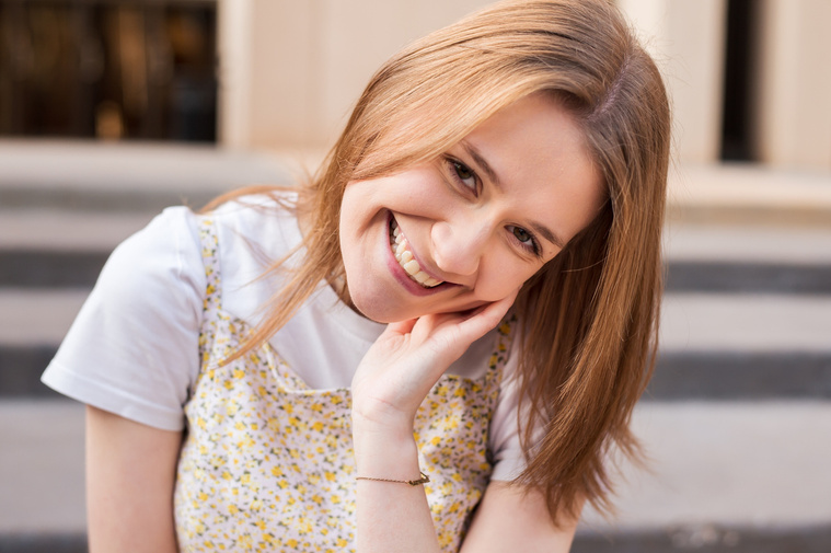 high school senior girl sits with her head to the side resting in her hand and smiles on the steps of a building in downtown Oklahoma City