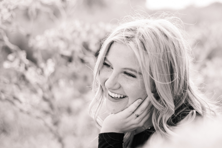 black and white photo of a high school senior girl sitting in a field in Oklahoma smiling to the side for her photo session