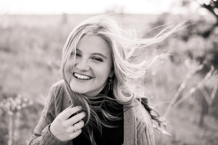 black and white image of a high school senior girl with her hair blowing in the wind smiling for her photo session in Oklahoma