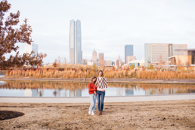 a mom and her teen daughter hugging and smiling at Scissortail Park with the Oklahoma City skyline behind them