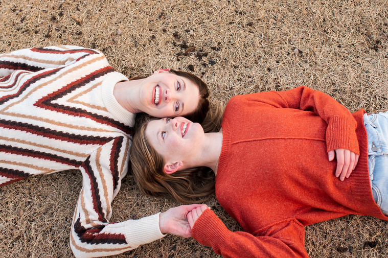 a mom and her teen daughter lay on their backs in the grass hold hands and smile at each other at Scissortail Park in Oklahoma City