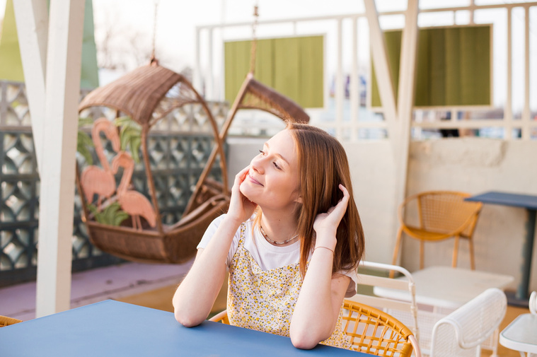 high school senior girl sits at an outside blue table and yellow chair at the Classen Inn in midtown Oklahoma City and smiles off to the side with her chin in her hands