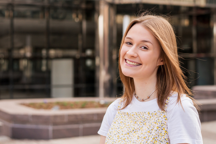 high school senior girl smiles cutely in front of an office building with reflective windows in downtown Oklahoma City