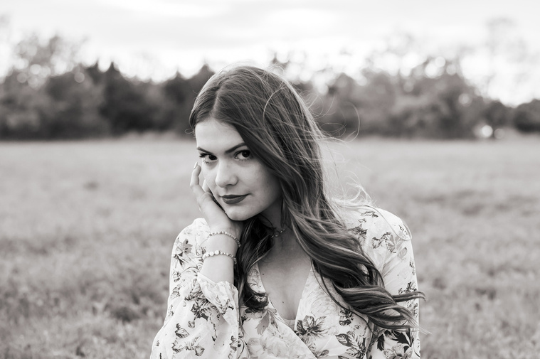 black and white photo of a high school senior girl dressed in boho style looking seriously at the camera with one hand on her face in Oklahoma City, Oklahoma