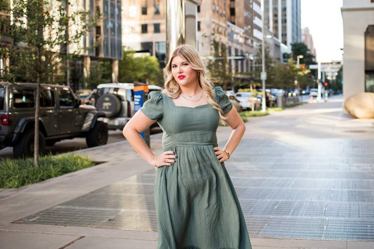 blond high school senior girl in a green dress has hands on hips and standing on a sidewalk in downtown Oklahoma City for senior portraits