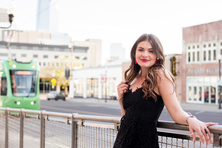 high school senior girl wearing a black dress standing against the streetcar pickup on the sidewalk in Automobile Alley in Oklahoma City, Oklahoma