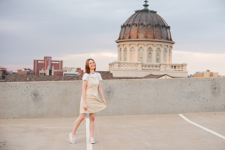 high school senior girl stands on the rooftop of a parking garage in midtown Oklahoma City and smiles 