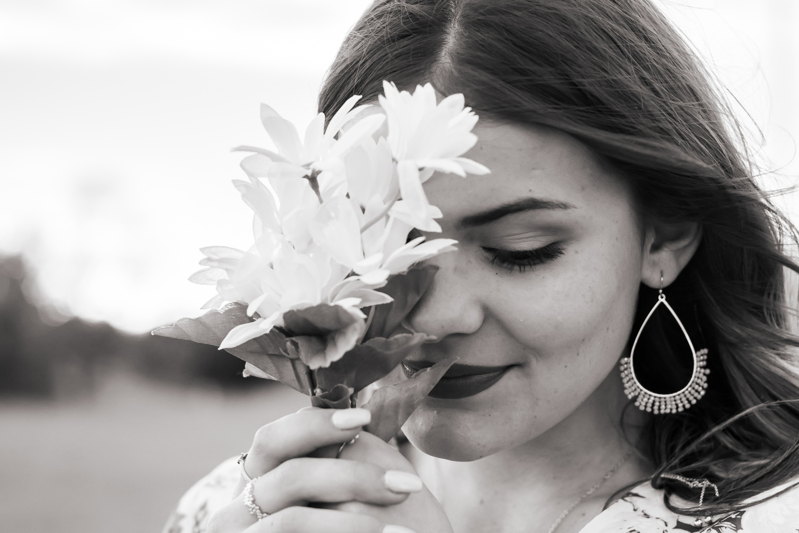 close up landscape black and white portrait of a senior girl holding a small bouquet of white flowers close to her face covering one eye and looking down in a field in south Oklahoma City