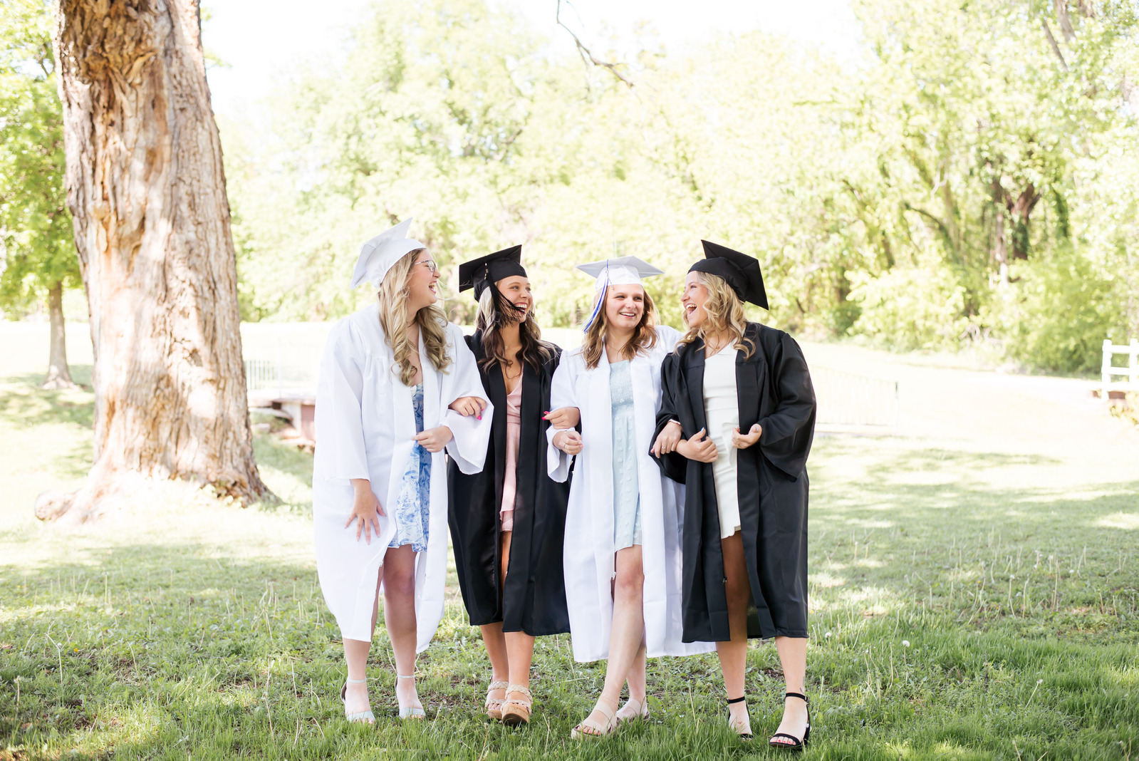 4 high school senior girls wearing their graduation caps and gowns walk together laughing in a park in Newcastle Oklahoma