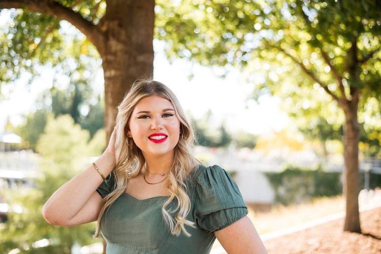 blond high school senior girl in a green dress has one hand in her hair and smiles brightly at Myriad Gardens in downtown Oklahoma City for senior portraits