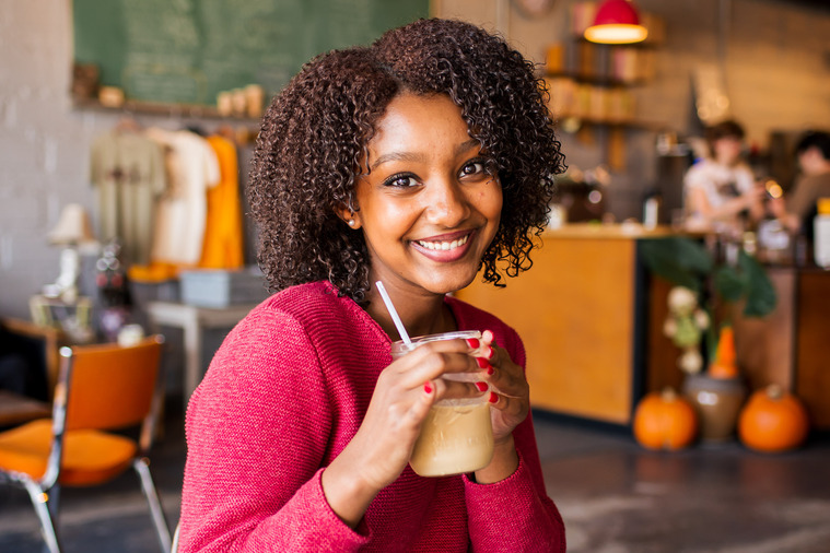 Ethiopian teen girl wearing a pink sweater sits in a coffee shop in Norman Oklahoma holding her iced coffee drink and smiling