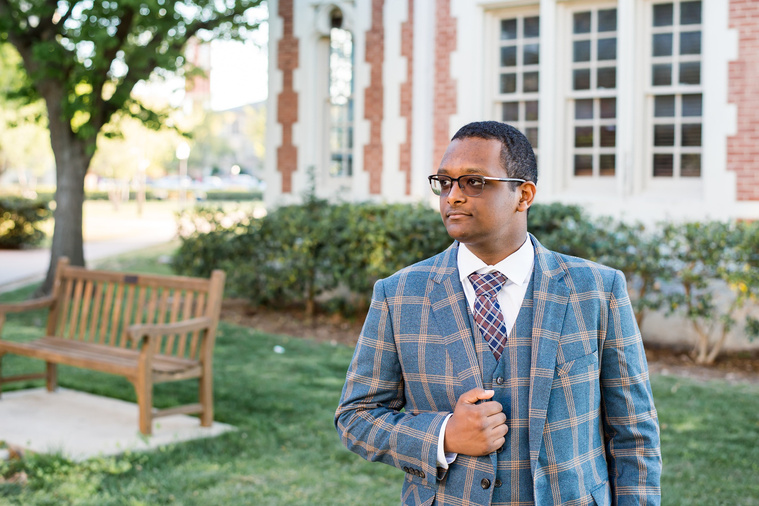 portrait of an african-american high school senior boy wearing a patterned suit holding his lapel and looking to the side in front of a building on the OU campus in Norman Oklahoma