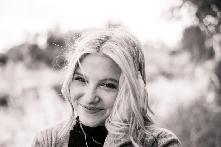 black and white photo of a high school senior girl scrunching her nose slightly and smiling while she holds her hair away from her face