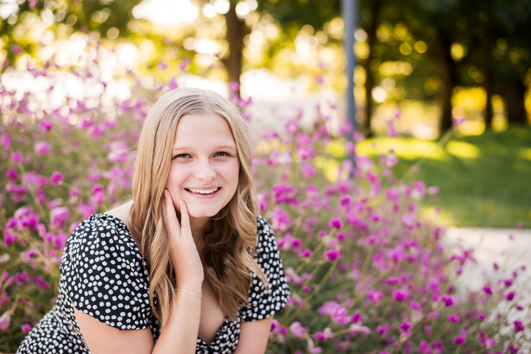 blond high school senior girl wearing a dress resting her chin in her hand sitting in front of pink flowers at Myriad Gardens in downtown Oklahoma City