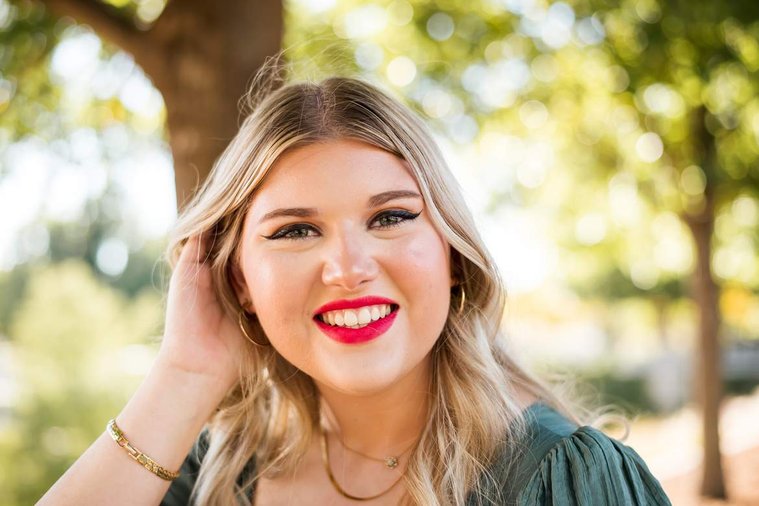 blond high school senior girl smiles brightly with one hand in her hair at Myriad Gardens in downtown Oklahoma City for senior portraits