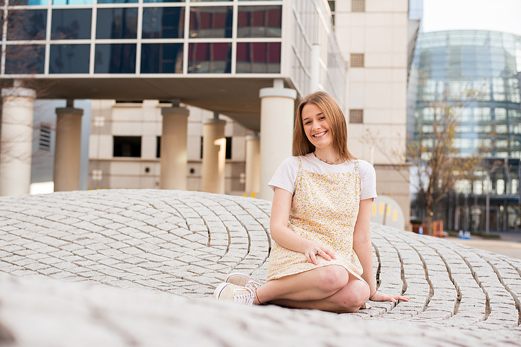 high school senior girl sits on a stone structure with the Devon tower in downtown Oklahoma City behind her